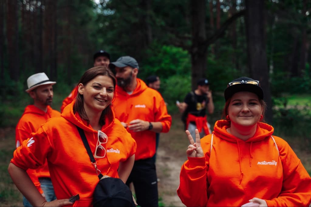 Naturaily employees smiling to the camera, while standing in the forest dressed in the Naturaily branded hoodies
