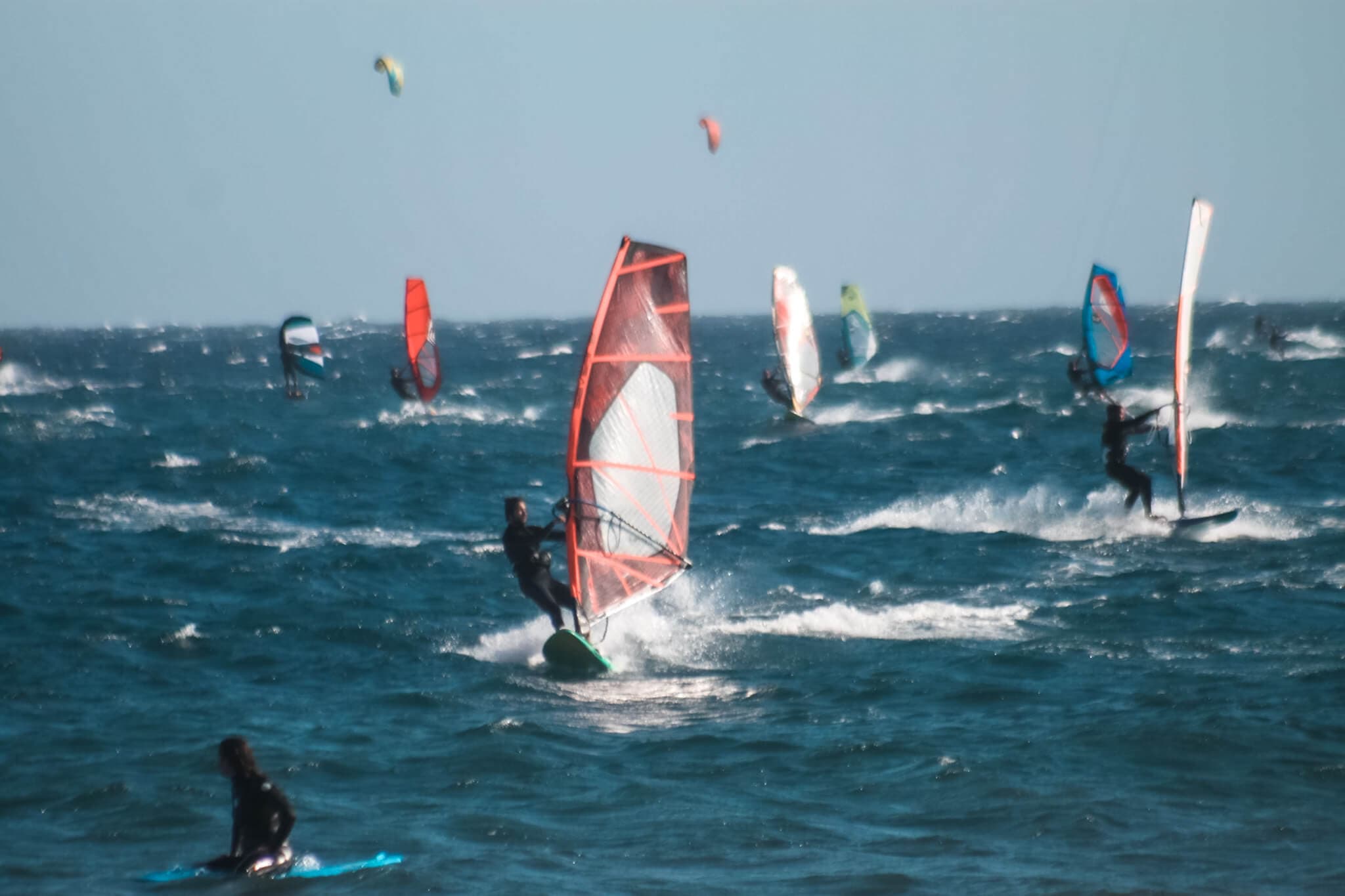 People windsurfing and kiteboarding on a choppy sea under a clear blue sky.