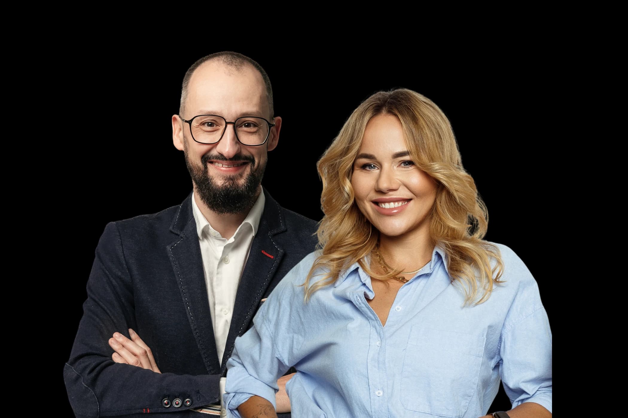 A man and woman smile at the camera. The man has glasses and a beard, wearing a suit. The woman has blonde hair, wearing a blue shirt.