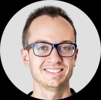 Mateusz - smiling man with short hair and glasses, wearing a dark shirt, against a light gray background.