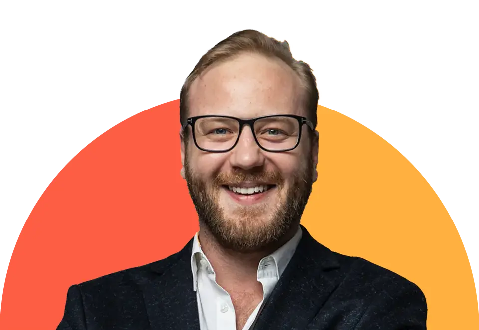 Smiling man with glasses and a beard, wearing a dark suit and white shirt, in front of an orange and yellow gradient background.