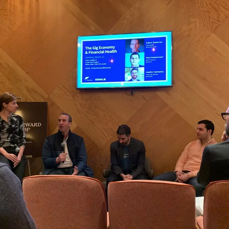 Panel discussion on "The Gig Economy & Financial Health" with four seated speakers and a moderator, screen displaying topic details.