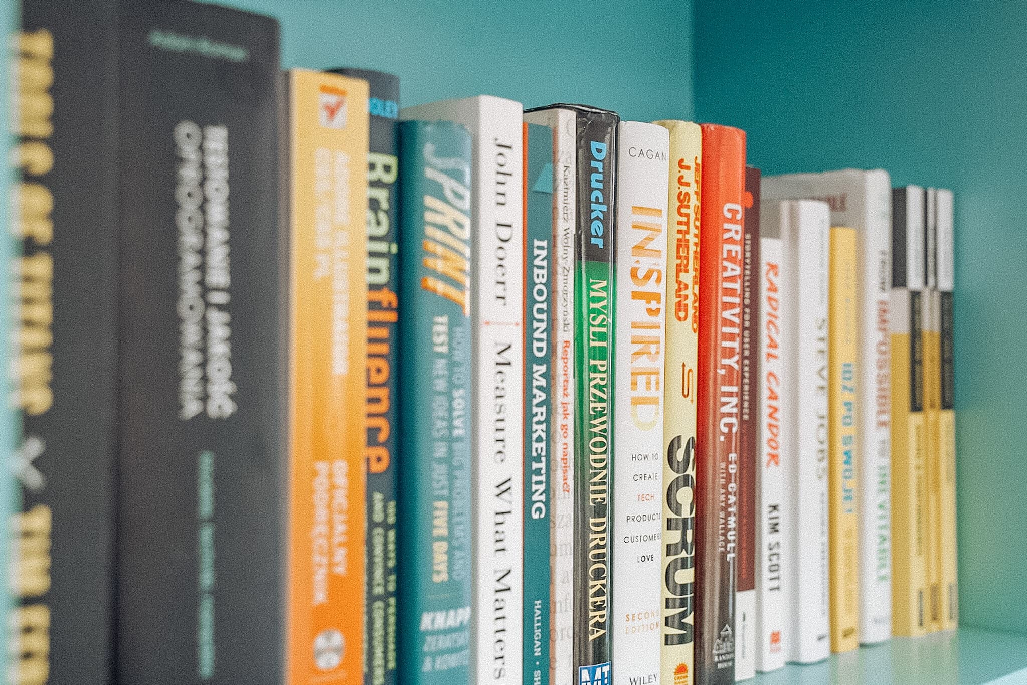 A row of diverse business and marketing books on a shelf, featuring titles like "Influence," "Scrum," and "Creativity, Inc."